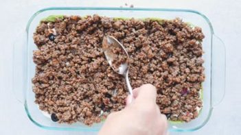 spooning ground beef in a casserole dish