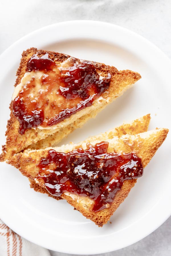 slices of keto toast topped with butter and strawberry jam on a white plate