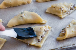 a brush spreading egg wash on chicken pot pie turnover