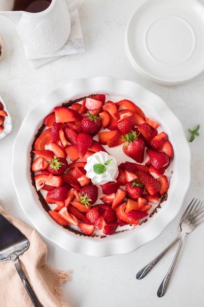 Overhead view of the finished strawberry cream pie in a white pie dish with whipped cream and fresh strawberries.