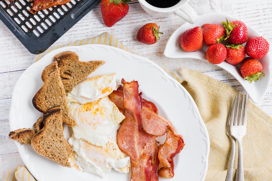 a breakfast platter with eggs, bacon, toast next to strawberries and coffee