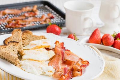 a plate of bacon, eggs and low carb toast next to fresh strawberries