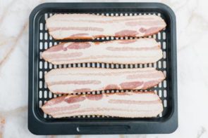 four slices of uncooked bacon on an air fryer tray