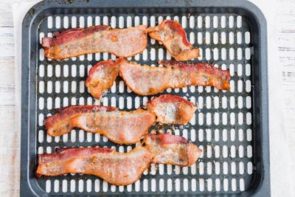 an air fryer tray with four slices of cooked bacon on it
