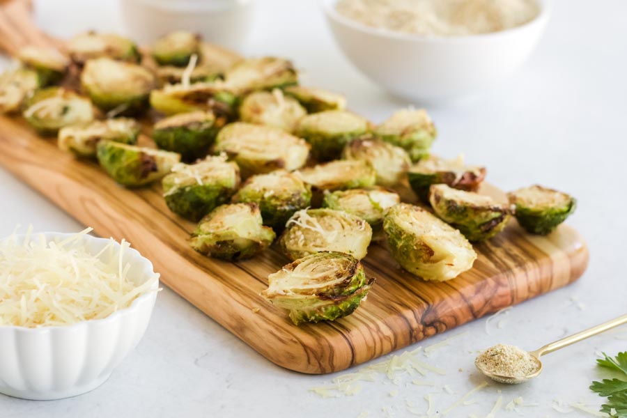 a bunch of brussels sprouts on a board with cheese and crumbs nearby