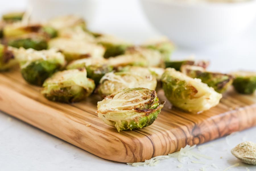 cooked brussels sprouts on a platter board with parmesan cheese shreds nearby