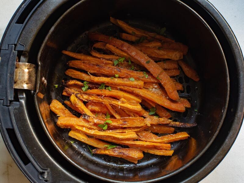 An air fryer basket filled with carrot fries perfectly roasted and topped with fresh herbs.