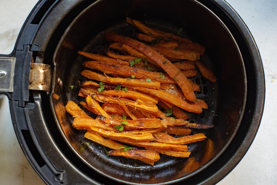 An air fryer basket filled with carrot fries perfectly roasted and topped with fresh herbs.
