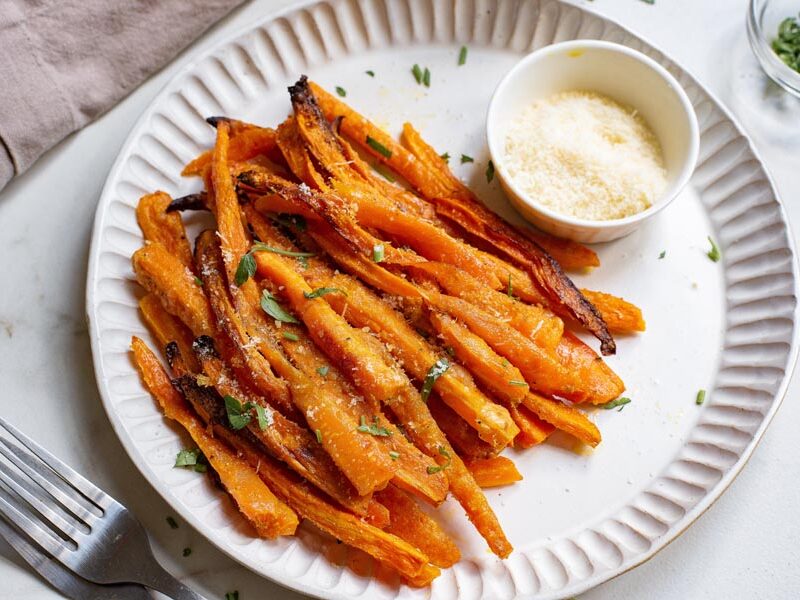 A plate with carrot fries next to freshly grated parmesan cheese in a bowl and two forks.