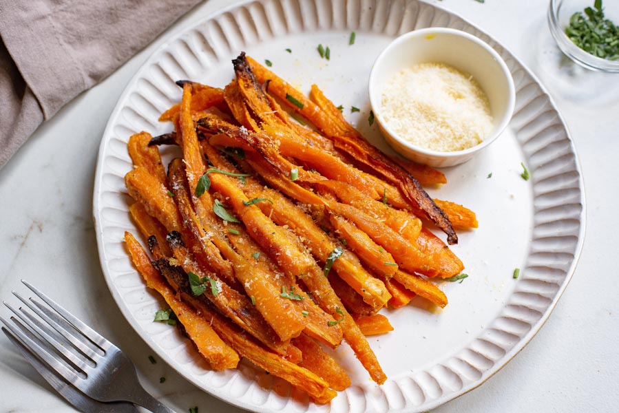 A plate with carrot fries next to freshly grated parmesan cheese in a bowl and two forks.