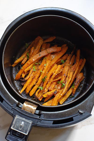 An air fryer basket with roasted carrots inside topped with herbs.