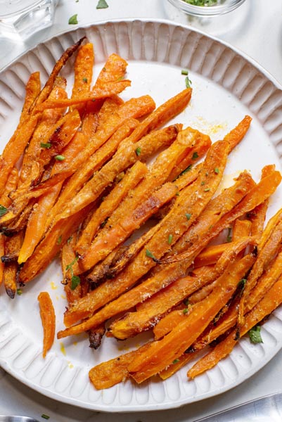 Carrot fries topped with herbs and parmesan cheese on a plate.