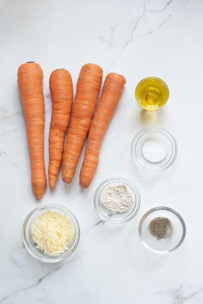 Four carrots next to a small bowl of olive oil and other small bowls with seasonings and parmesan cheese inside.