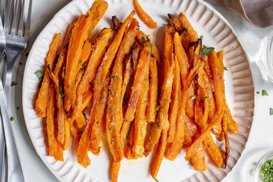 Long carrot fries on a white plate topped with herbs and next to forks.