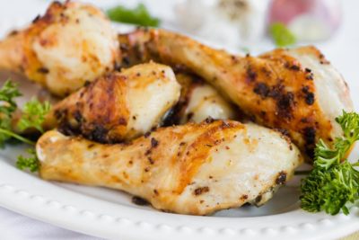 a group of roasted chicken legs on a plate with parsley and crispy garlic bits