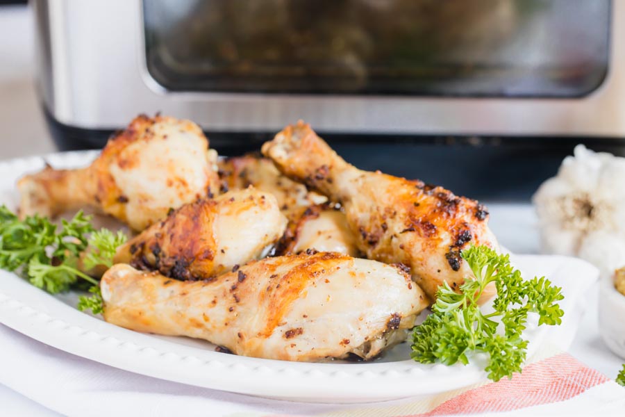 a platter of juicy chicken drumsticks on a plate by an air fryer