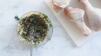 a bowl with a buttery marinade next to drumsticks