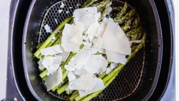 parmesan cheese on top of asparagus in an air fryer basket