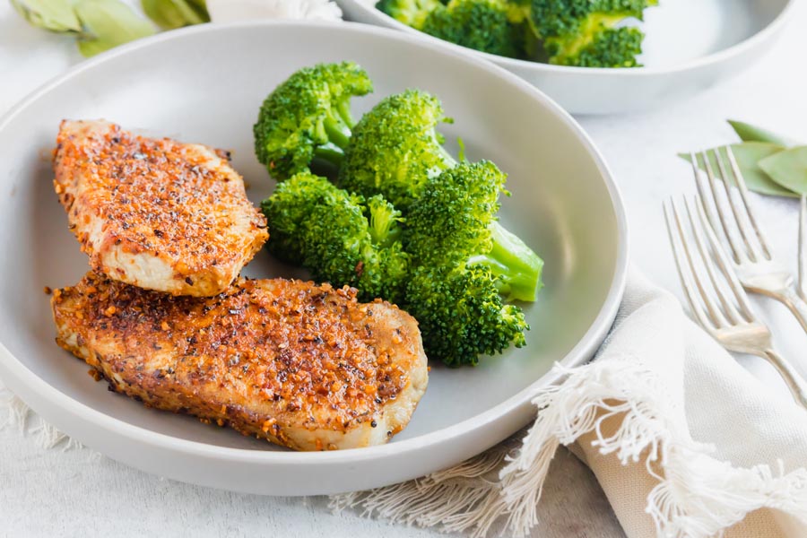 Two cooked boneless pork chops on a dinner plate next to steamed broccoli.