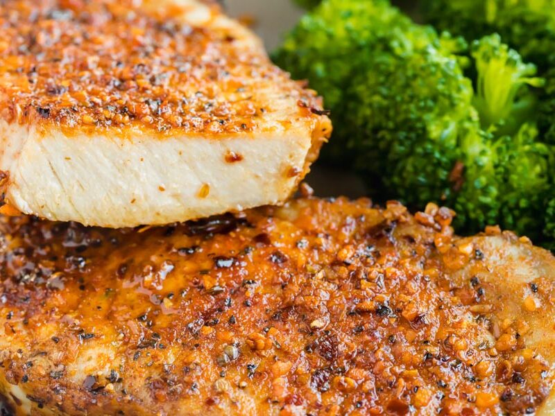 A pork chop cut in half to show how juicy it is. Next to broccoli.