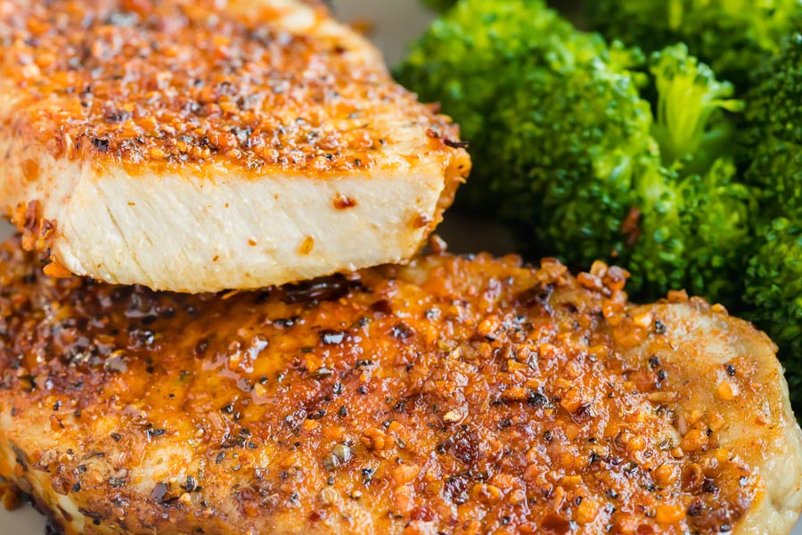 A pork chop cut in half to show how juicy it is. Next to broccoli.