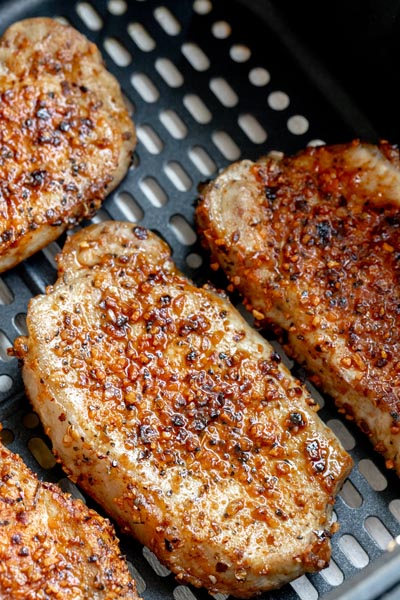 Juicy pork chops in an air fryer basket seasoned with chunky seasoning all over.