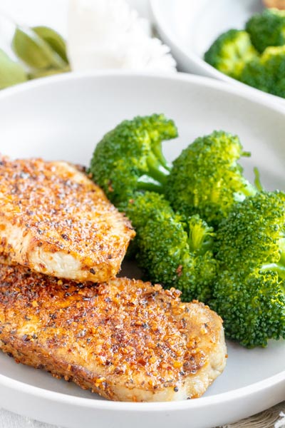 A dinner plate with two seasoned pork chops on it next to broccoli.