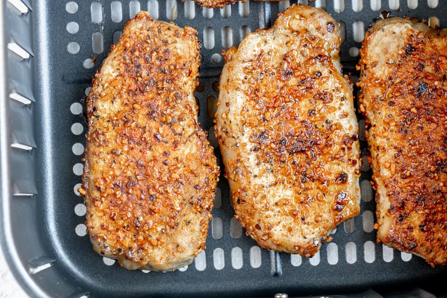 Three juicy, roasted pork chops cooked in an air fryer basket and heavily seasoned.