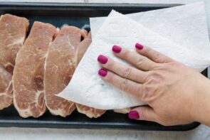 Patting dry boneless pork chops with a paper towel.