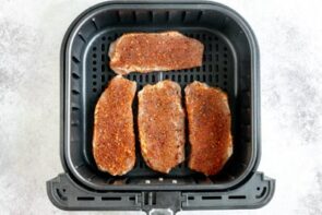 Looking down into an air fryer basket with four raw pork chops inside.