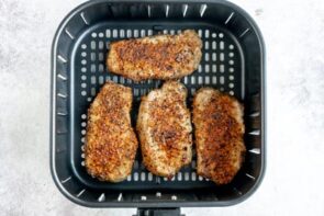Looking into an air fryer basket with four seasoned and cooked pork chops inside.