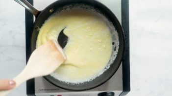 stirring a cream sauce in a skillet with a wooden spoon