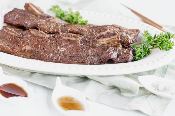 short ribs on a white platter with sauces next to it