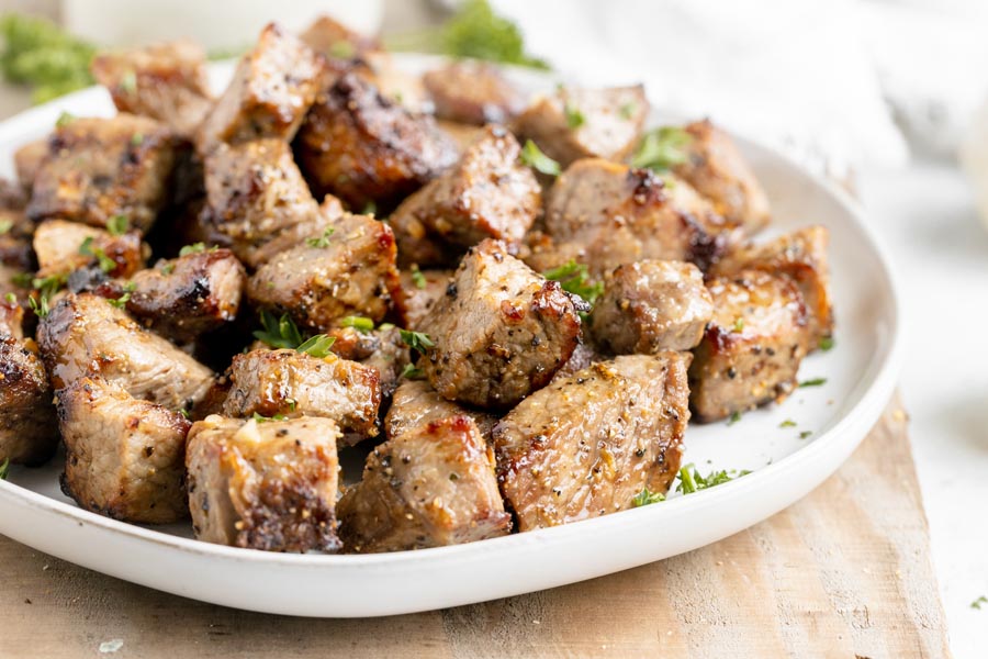 A plate filled with juicy steak bites topped with parsley.