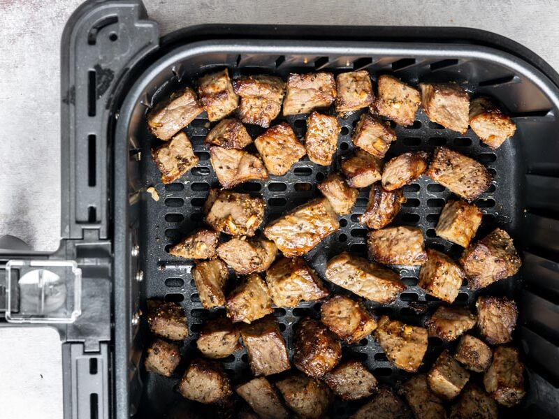 An air fryer basket with cooked steak bites inside.