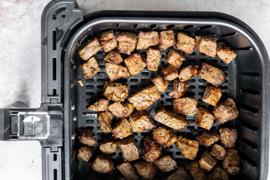 An air fryer basket with cooked steak bites inside.