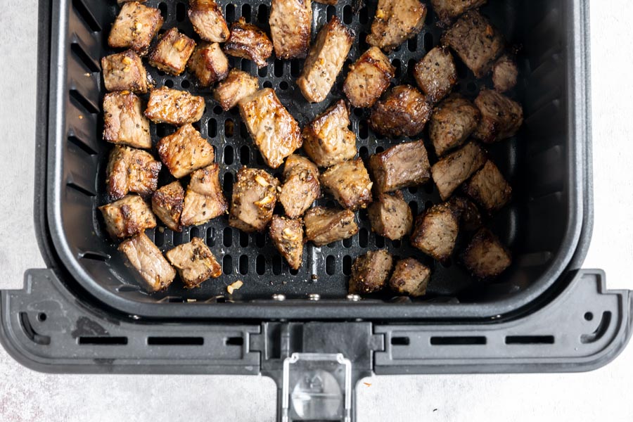 An air fryer basket filled with juicy steak bites.