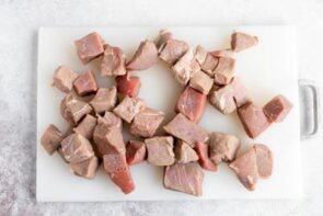 A cutting board with cut up chunks of steak.