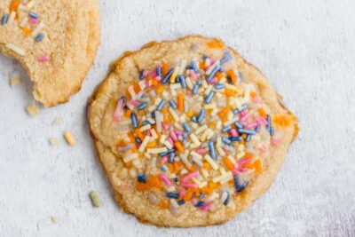 A whole cookie topped with multi-colored sprinkles.