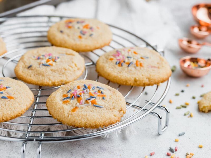 Cookies on a wire rack topped with sprinkles with sprinkles nearby.