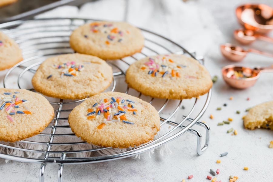 Cookies on a wire rack topped with sprinkles with sprinkles nearby.