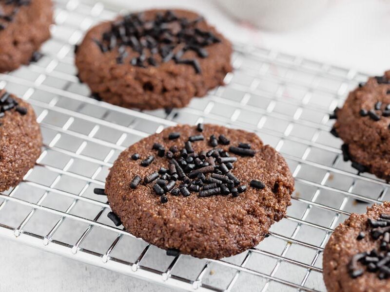 Chocolate cookies topped with sprinkles on a wire rack.