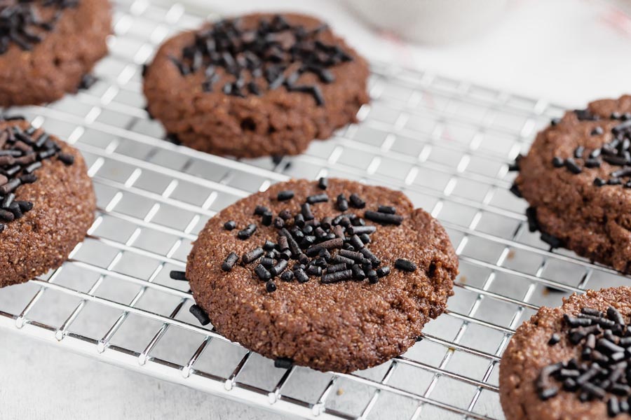 Chocolate cookies topped with sprinkles on a wire rack.