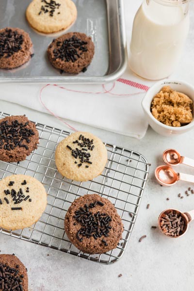 Cookies on a cooling rack and a baking tray with milk, brown sugar and sprinkles nearby.