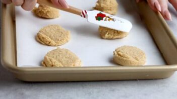 Using a Christmas spatula to flatten cookies on a baking tray.