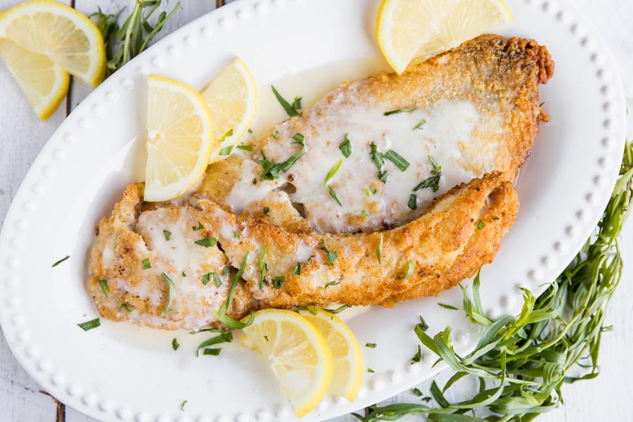 overhead view of fried pacific rockfish on a plate with lemon slices and topped with a sauce