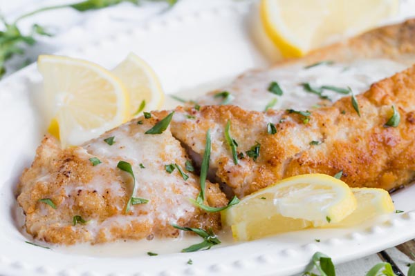 lemon cream sauce poured all over juicy almond crust rockfish fillets on a plate with fresh tarragon
