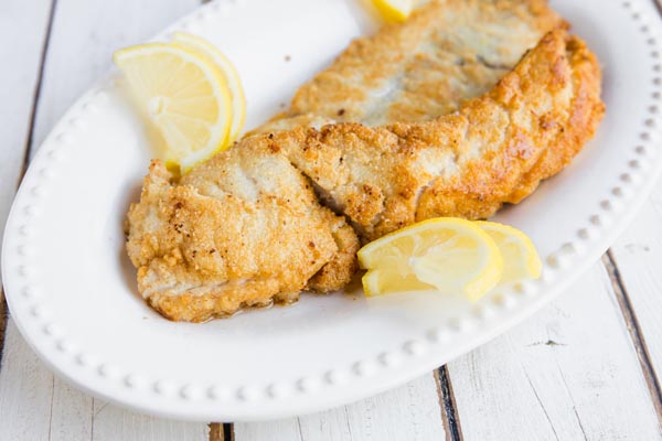 a golden crust on several rockfish fillets on a plate with some lemon slices
