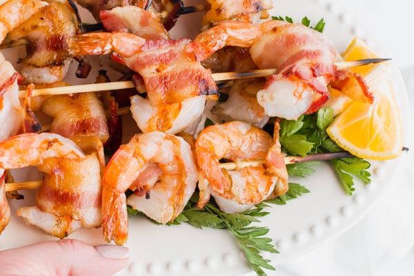 bacon wrapped shrimp on skewers lined up on a plate