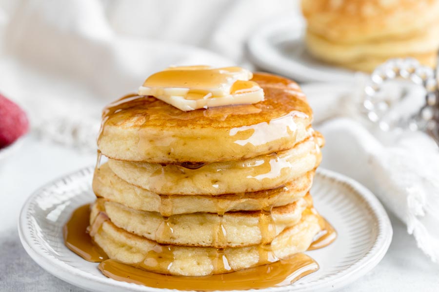 Five pancakes stacked on a plate, covered with syrup and topped with butter.